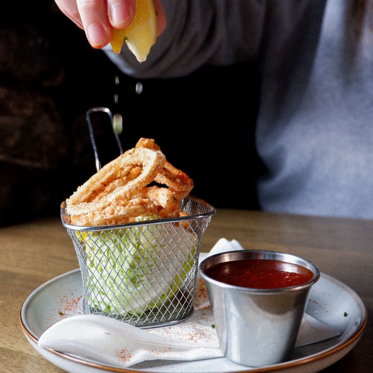Calamari in a wire basket with a hand squeezing lemon over it