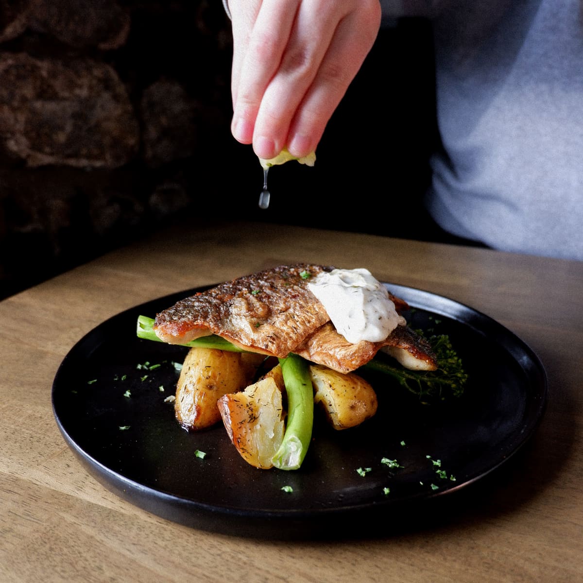 Pan-fried fish fillet with potatoes and green beans, a hand squeezing lemon over it