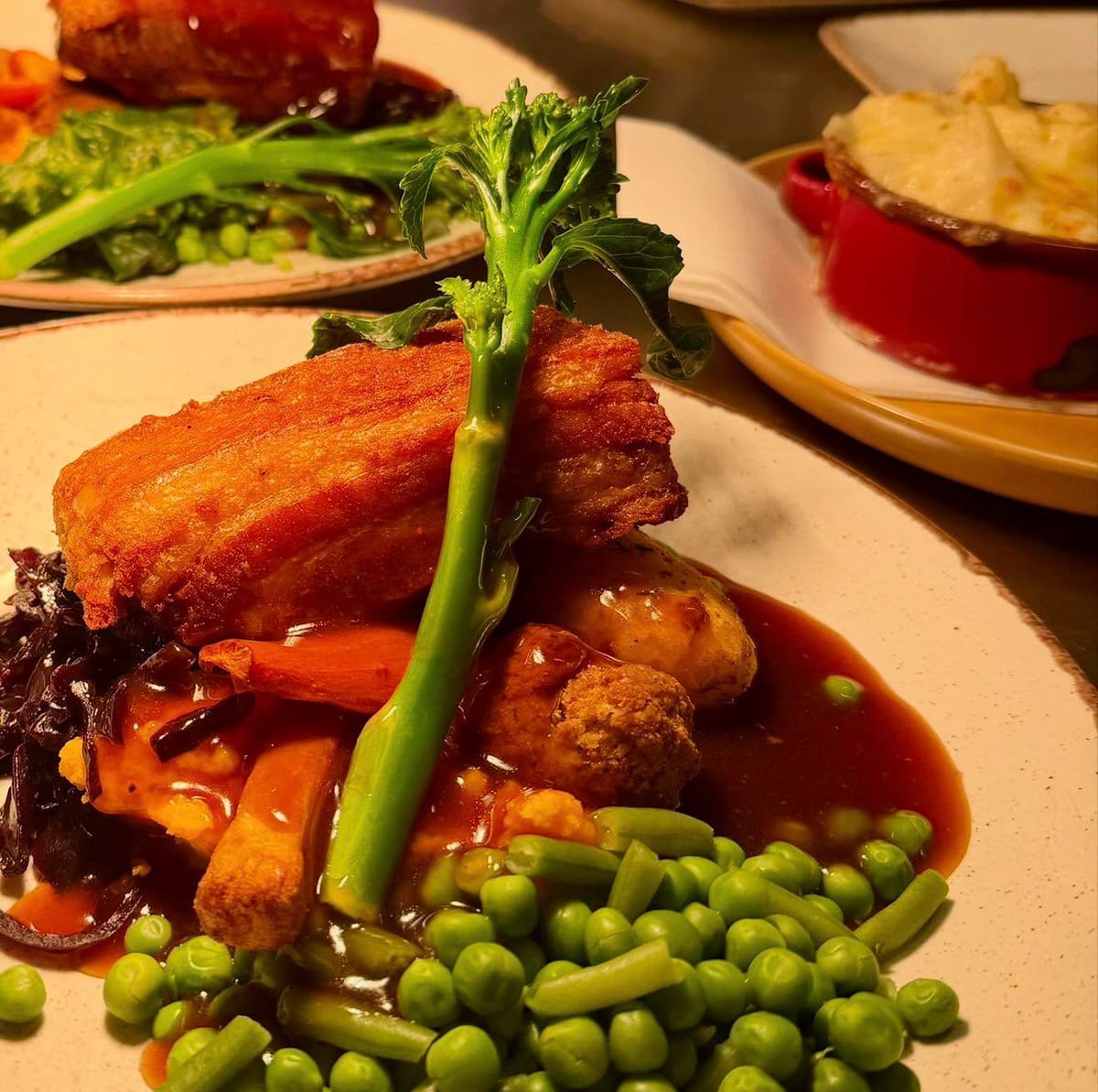 Crispy pork belly with gravy, red cabbage, carrot and peas on a cream plate