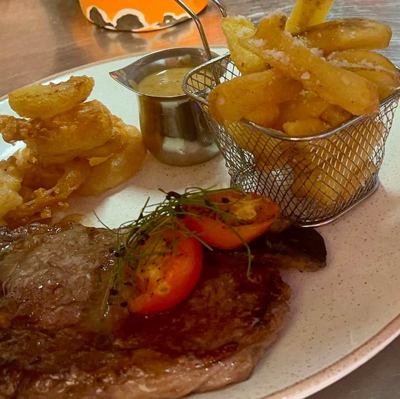 Steak with chips in a wire basket and a grilled tomato