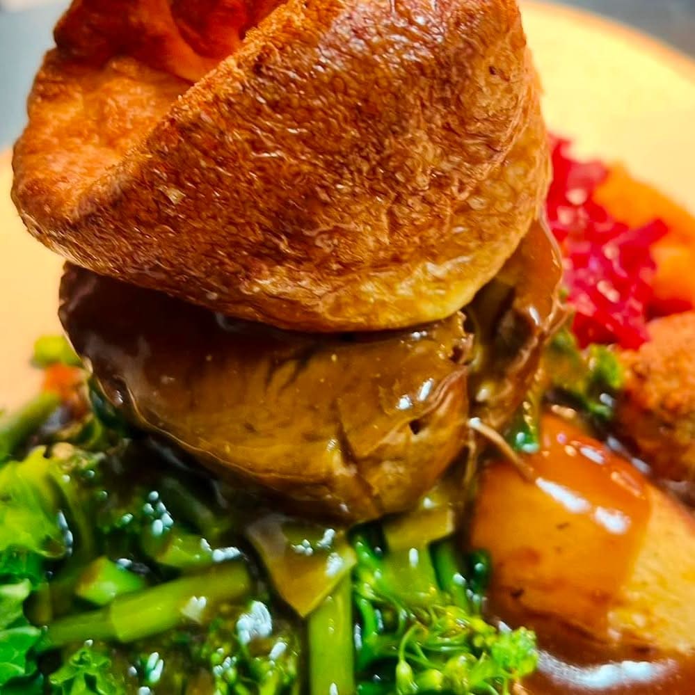 A roast dinner topped with a large Yorkshire pudding, with greens