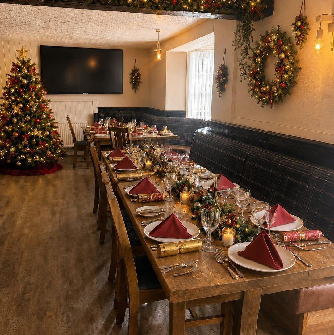 The dining room at The Ship Inn laid for Christmas, with a long table, red napkins, crackers, wreaths and a Christmas tree
